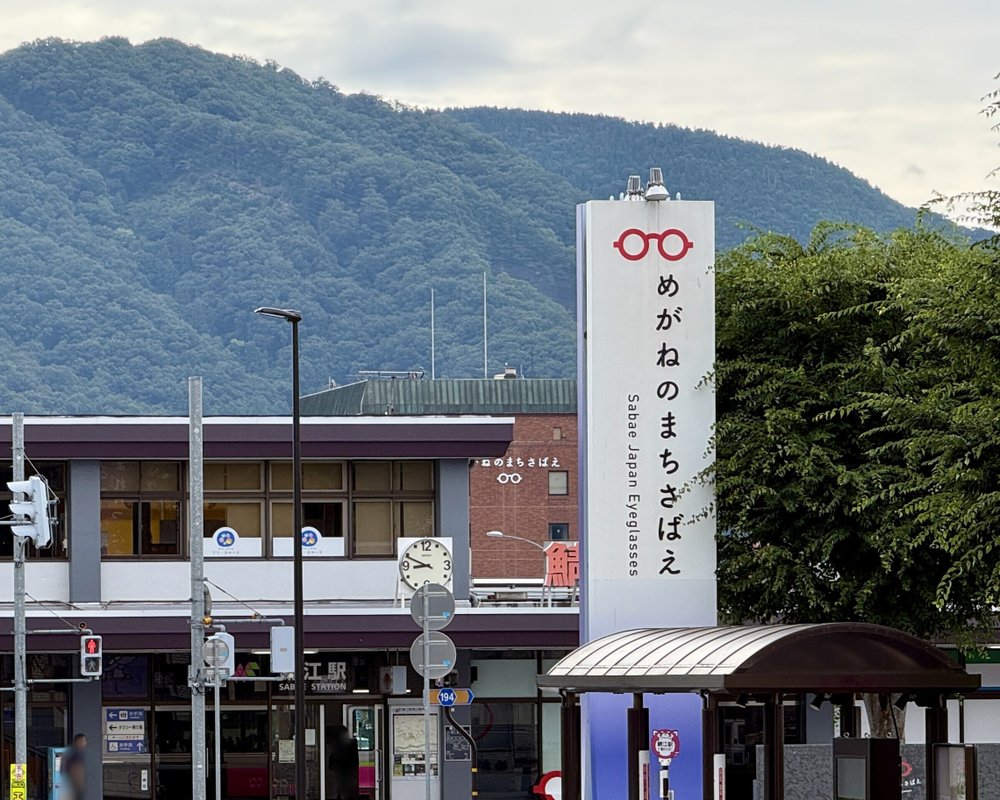 鯖江駅と「めがねのまちさばえ」の塔、うしろに山並み